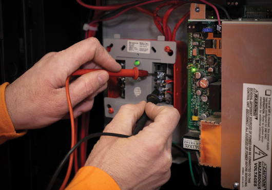 A fire alarm technician with High Rise Security Systems, LLC measures voltage with a digital volt meter to troubleshoot a communications failure.