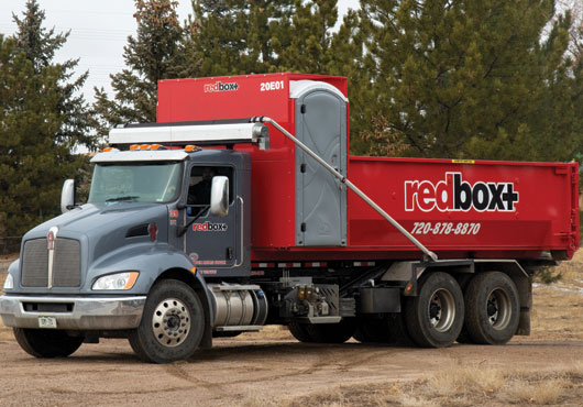 A redbox+ patented dumpster and portable toilets being delivered to a job site.