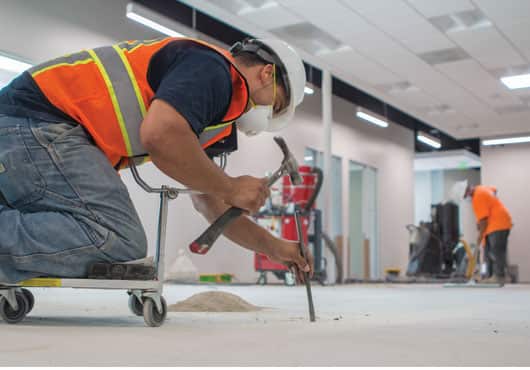 Veteran Solutions Inc. team member breaks out an old patch of flooring to ensure the moisture barrier is bonded directly to the concrete.