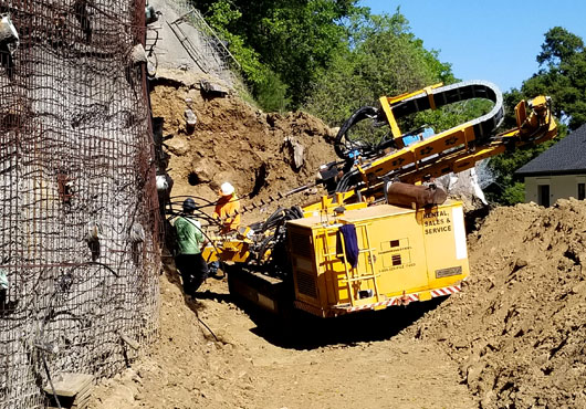 Geo Grout Ground Modification Specialists, Inc. drills anchors for soil stabilization next to a subdivision.