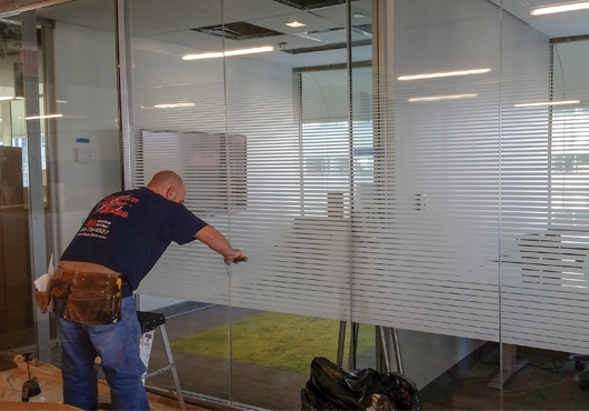 Eastern Solar Glass employee John DeLuca installs a band of lined film to allow a limited view of the area beyond the glass.  
