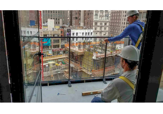 Matt Long and Kyle Stanley of AVCON Commercial Railing Systems, LLC install a HorizAL by AVCON glass-and-slab-cover railing system on the balcony for a Leeding Builders Group building project in New York City.