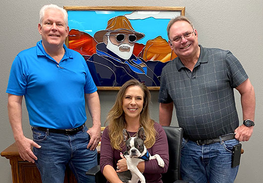 The leaders and co-owners of Decca Builders, Inc. in front of a stained-glass portrait of their father, Darryl Wareing, who founded the company in 1984 and passed away in 2005. Left to right: Michael Wareing, President; Kristen “Kris” Zeno, CFO (with her dog, Nugget); and John Wareing, Vice President.