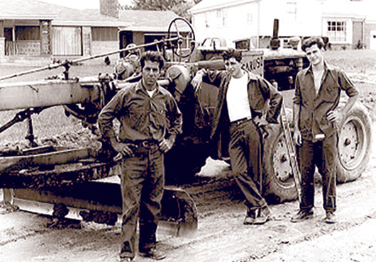 Left to right: Peter Caruso Paving Founder/President Peter Caruso II poses with sons and successor Presidents Peter Caruso III and John Caruso by a road grader on a housing development site during the mid-1960s. 