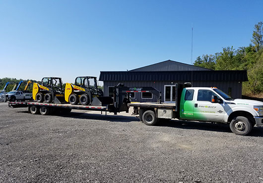 Priority Equipment Rental delivers skid steers to a job site. 