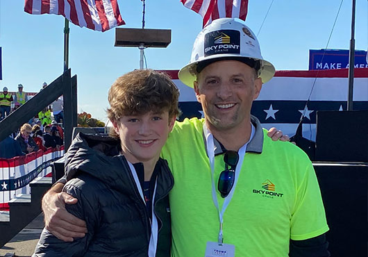 For a presidential address in Butler, PA, Managing Partner Dave Brocious (right) and his son Evan pose before flags hoisted by Sky Point Crane.