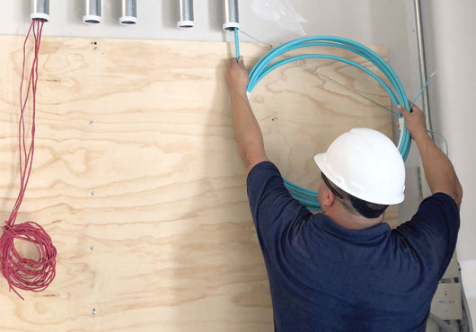 Project lead Teofilo “Teo” Rodriguez maintaining the correct fiber bend radius while feeding cable into a conduit at Fresh Creative Foods.