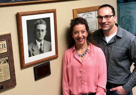 Dahl Glass President Gabe Rees (right) with his wife, Heidi, in the company’s office surrounded by historic photographs of company founder, Ole Dahl, along with a photo of the company’s original shop in Silverdale, WA.